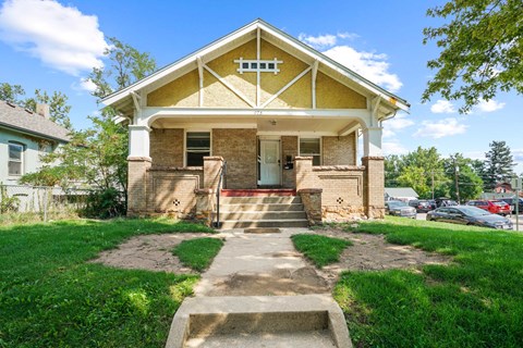 A yellow house with a white porch and a small front yard.